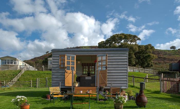This shows the hut with the double doors open so you can see the kitchen with a Belfast sink.  and the outside seating area.  There is a table, bench